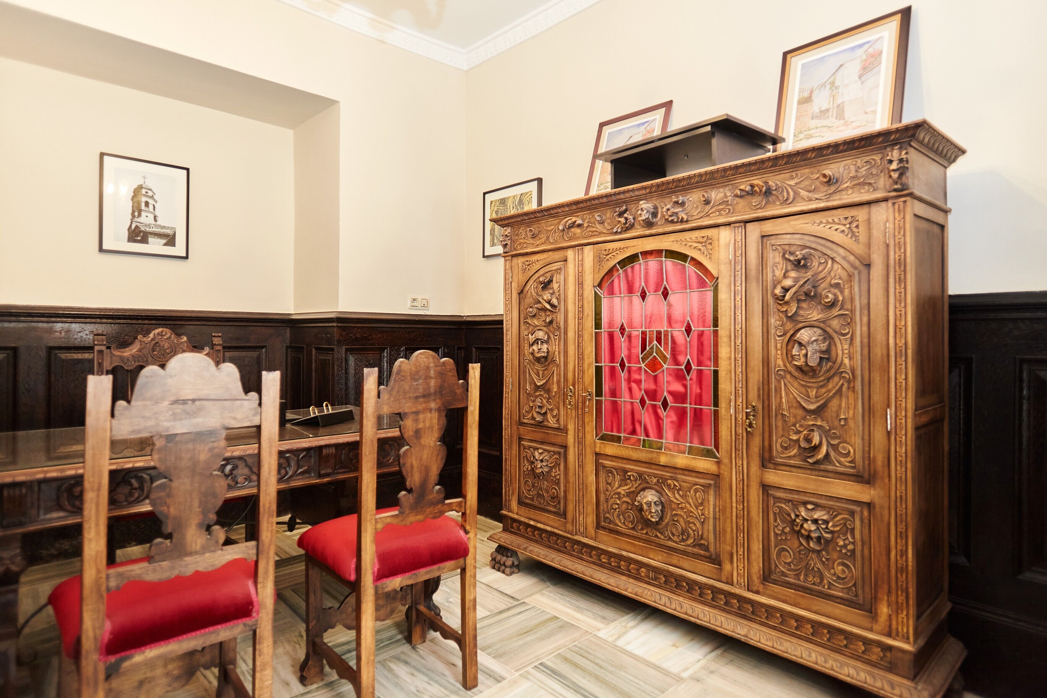 Une pièce avec un meuble en bois, deux chaises dotées de coussins rouges et un tableau encadré accroché au mur.