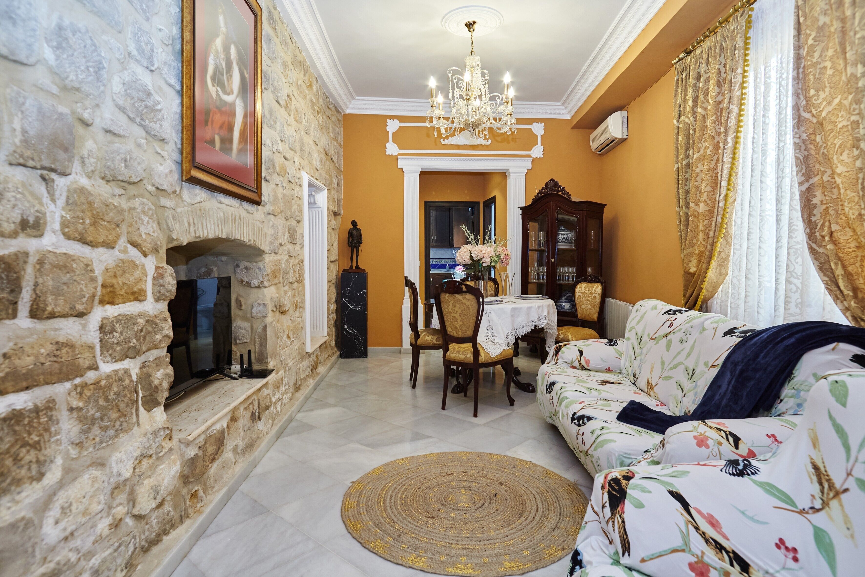 A living room with a stone fireplace, a chandelier, a sofa, and a dining area.