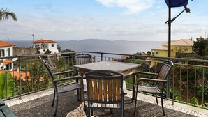 A terrace with a table and chairs, overlooking a coastal view. - Holiday Home "Casa T2" with Sea View, Private Terrace & Wi-Fi (Gaula)