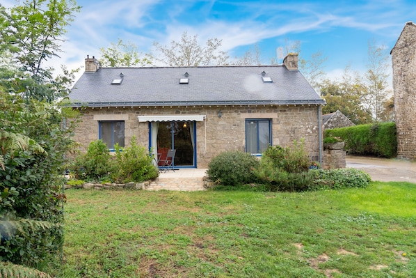Une maison en pierre avec un toit en pente, un porche à l’avant et un petit jardin.