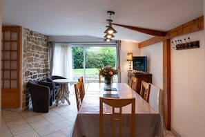 Un coin repas comprenant une table, des chaises, un vase avec des fleurs, un téléviseur et un mur en pierre.