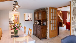 Un comedor con una mesa, sillas, un jarrón de flores, un armario y una escalera que lleva a otra habitación.