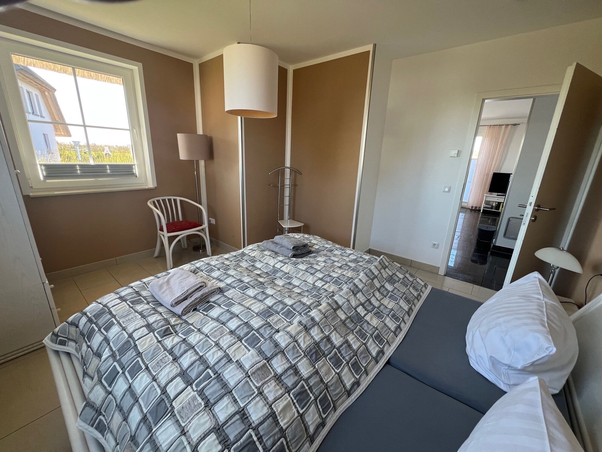 Una camera da letto con un letto, una sedia, un comodino, una lampada e una finestra.