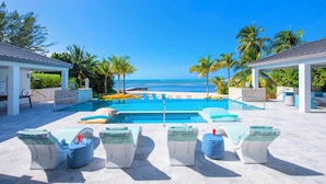 A pool area with lounge chairs, a view of the ocean, and palm trees. - Sun Rays by Grand Cayman Villas (Cayman Kai)