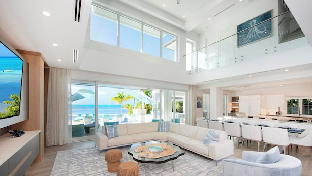 A spacious living area with a large window overlooking the ocean, a modern kitchen, and a dining area. - Sun Rays by Grand Cayman Villas (Cayman Kai)