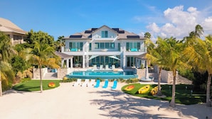 A large two-story house with a swimming pool, surrounded by palm trees and a sandy beach. - Sun Rays by Grand Cayman Villas (Cayman Kai)