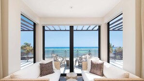 A balcony with white sofas and round tables, overlooking a beach and the ocean. - Rip Kai by Grand Cayman Villas (Rum Point)