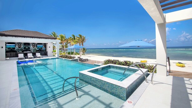 A pool area with a view of the ocean, a hot tub, and lounge chairs. - Rip Kai by Grand Cayman Villas (Rum Point)
