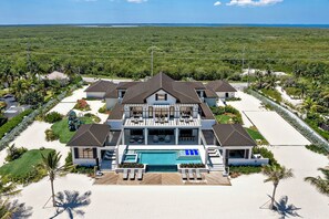 A large, multi-story beachfront property with a swimming pool, multiple balconies, and a well-maintained garden.