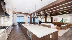 A spacious kitchen with a large island, wooden cabinets, and a view to the outside. - Rip Kai by Grand Cayman Villas (Rum Point)