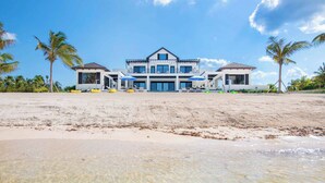 A beachfront property with a large house, clear waters, and palm trees. - Rip Kai by Grand Cayman Villas (Rum Point)