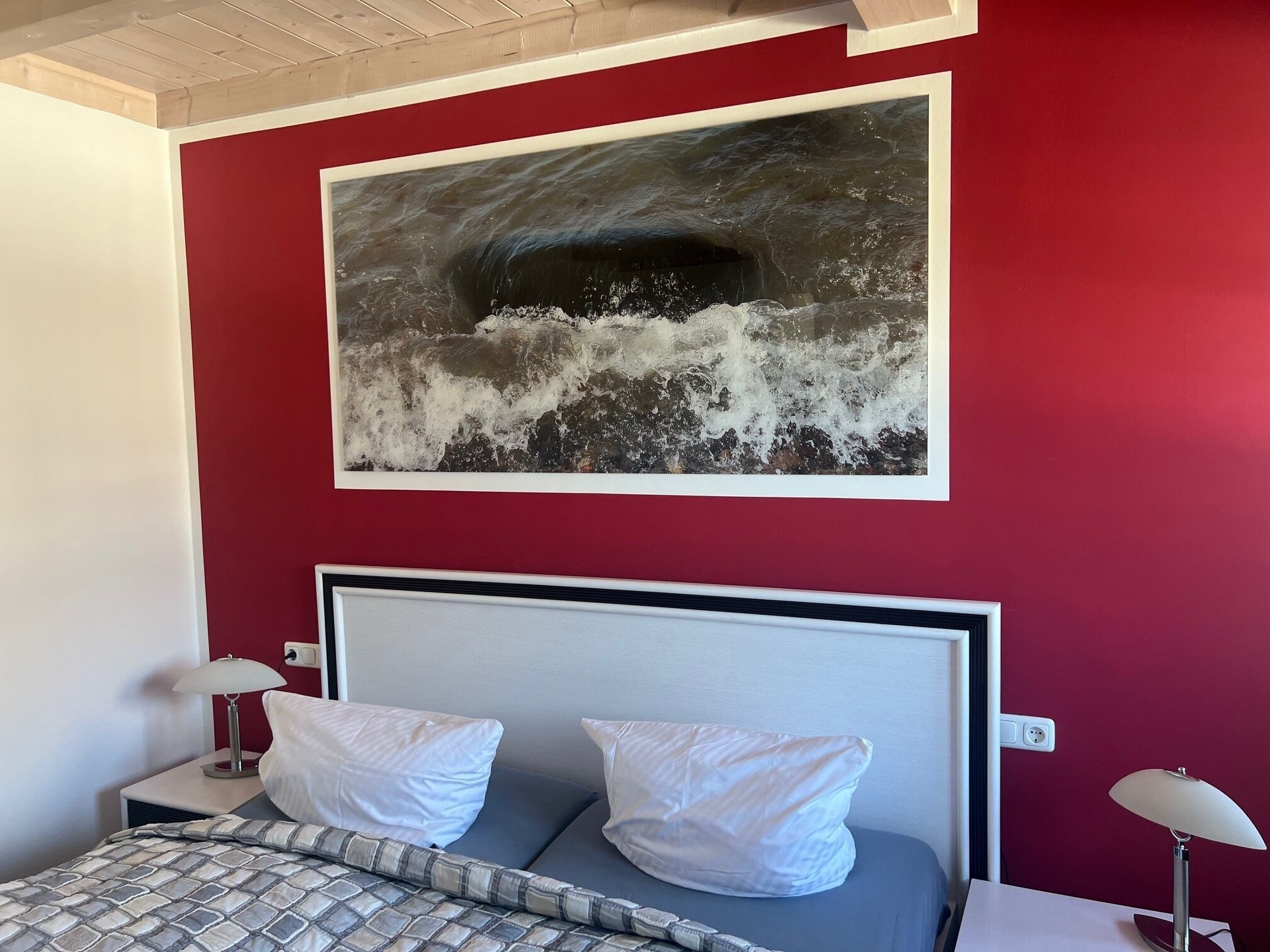 Une chambre d’hôtel avec un lit, deux tables de chevet et un grand tableau représentant une vague accroché au mur.