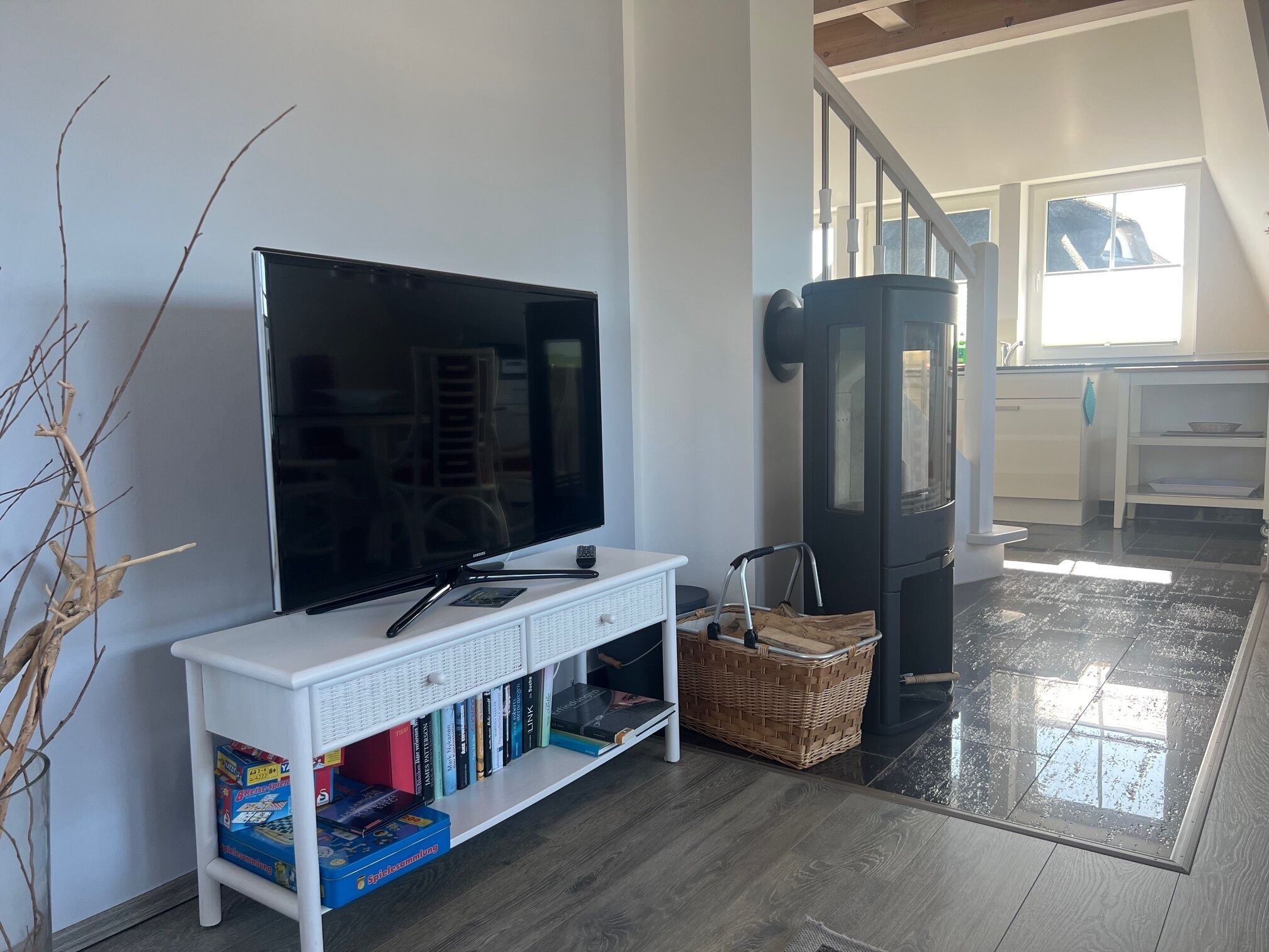 Un salon avec un téléviseur à écran plat posé sur un meuble blanc, une bibliothèque remplie de livres, un panier en osier et un radiateur noir.