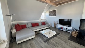 Un salon moderne avec un canapé d’angle gris, une table basse blanche, un téléviseur à écran plat et une cheminée.