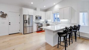Una cocina moderna con armarios blancos, electrodomésticos de acero inoxidable y una isla central con taburetes de bar.