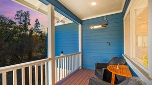 Un porche cubierto con fachada azul, muebles de mimbre y vista a árboles.