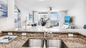 Una cocina moderna con encimeras de granito, un lavamanos de acero inoxidable y una zona de comedor con mobiliario blanco.