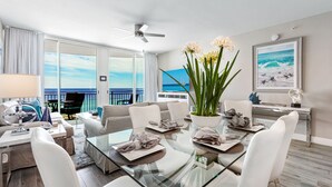 Una sala de estar moderna con una mesa de vidrio, muebles blancos y vista al océano.