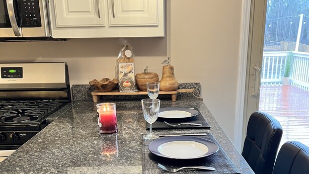 A kitchen with a granite countertop, a built-in stove, white cabinets, and a dining area with a black chair and a candle. - Nice family home (Hiram)