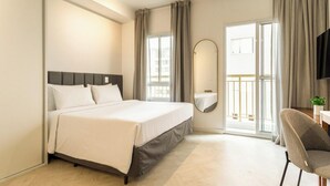 Habitación de hotel con una cama grande, un escritorio con silla, un espejo y un balcón con cortinas.