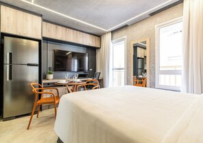 A modern hotel room with a large bed, a kitchenette with a refrigerator and stove, a dining area with chairs, and a large window. -  Smart Charlie Mobi Pinheiros (São Paulo)