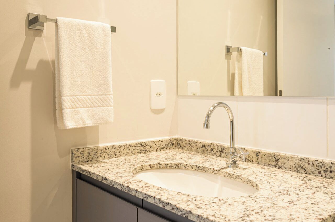 A bathroom with a granite countertop sink, a mirror, and a towel hanging on a metal towel rack.