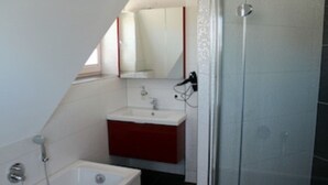 Ein kleines Badezimmer mit einem weißen Waschbecken, einem roten Schrank, einem Spiegel und einer Duschkabine.