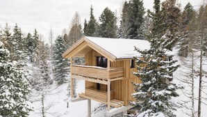 Una cabaña de madera con balcón, rodeada de árboles cubiertos de nieve.