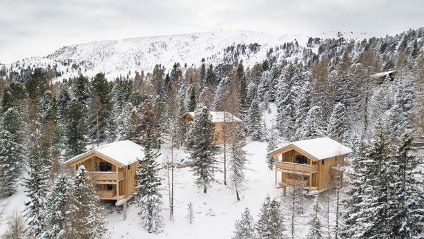 Una cabaña de madera con techo nevado, rodeada de un bosque.