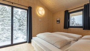 Una habitación de cabaña de madera con una cama, ventanas amplias y una lámpara fijada a la pared.