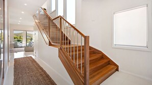 Una escalera moderna con escalones de madera y barandillas de metal, que conduce a una habitación con ventanas grandes y vistas al exterior.