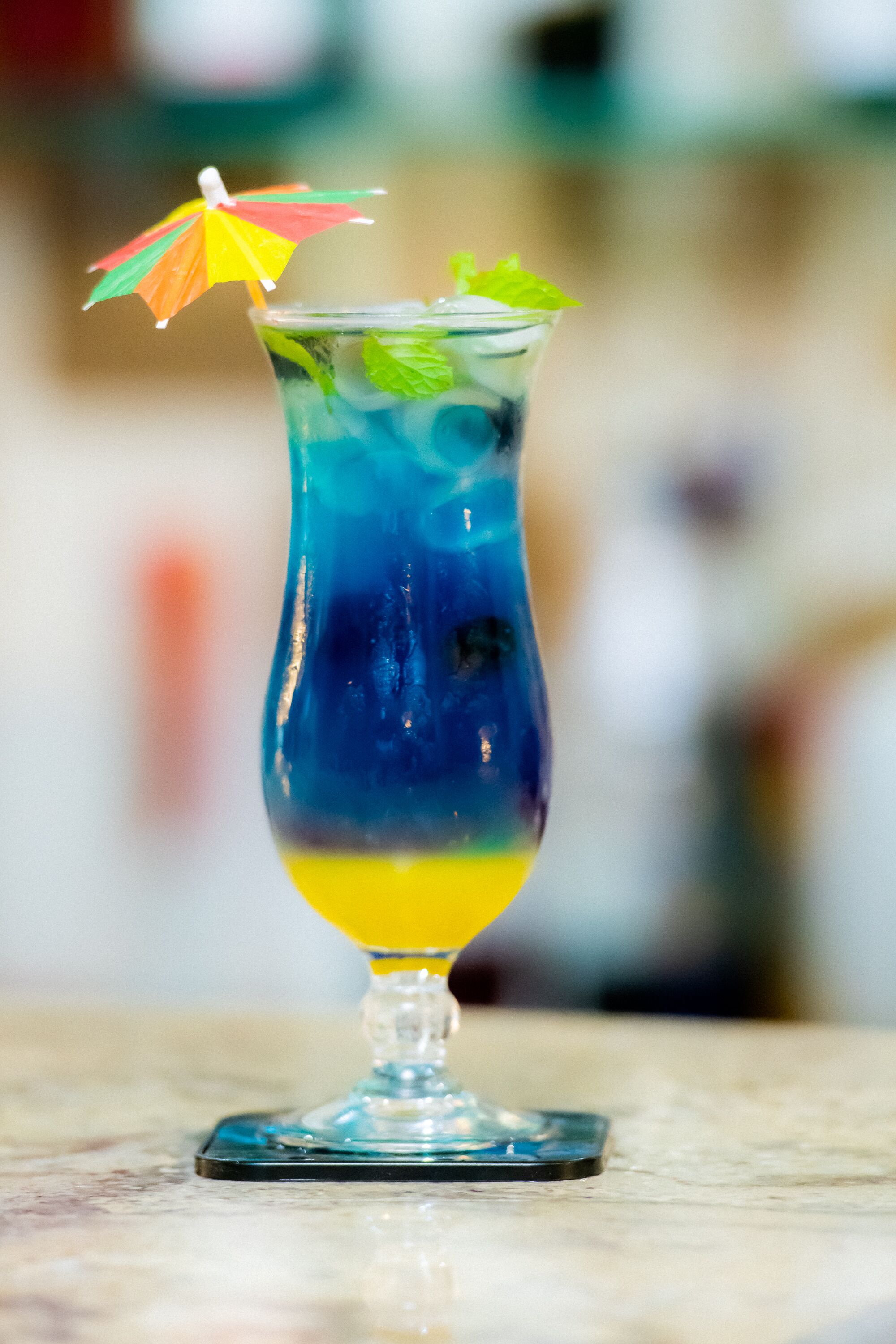 A tall glass with layered drinks and a colorful umbrella on top.