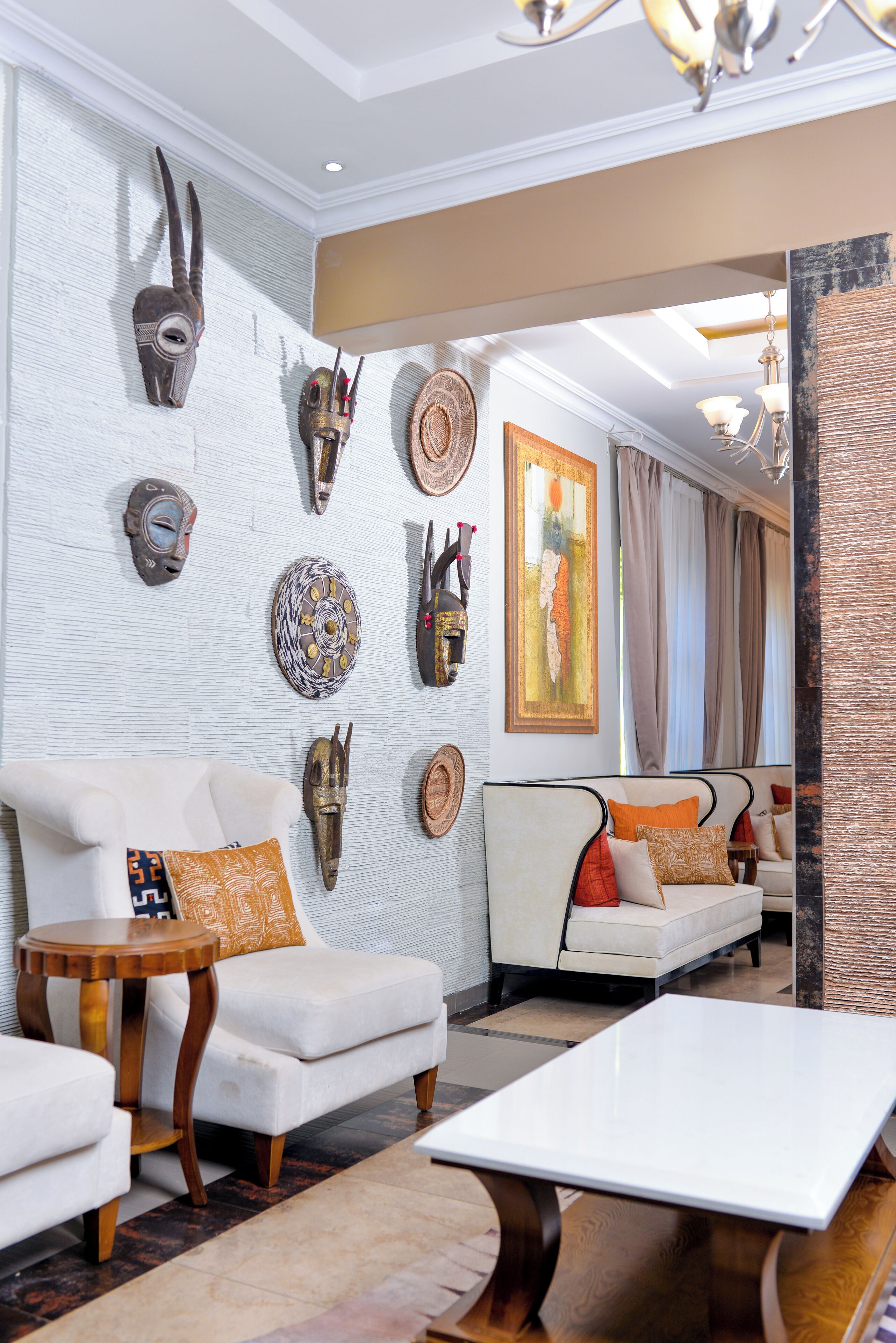 A modern living room with a white sofa set, a coffee table, and decorative masks on the wall.
