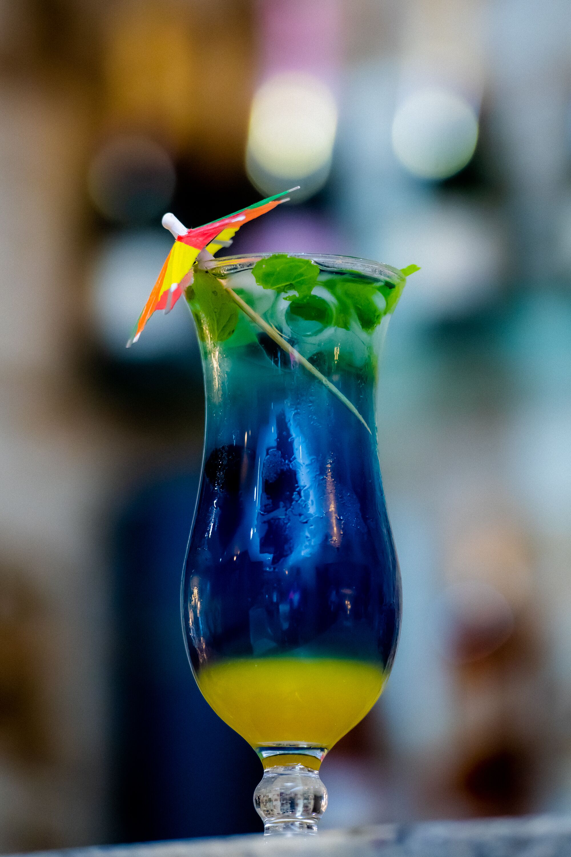 A cocktail in a glass with a colorful umbrella and mint leaves.