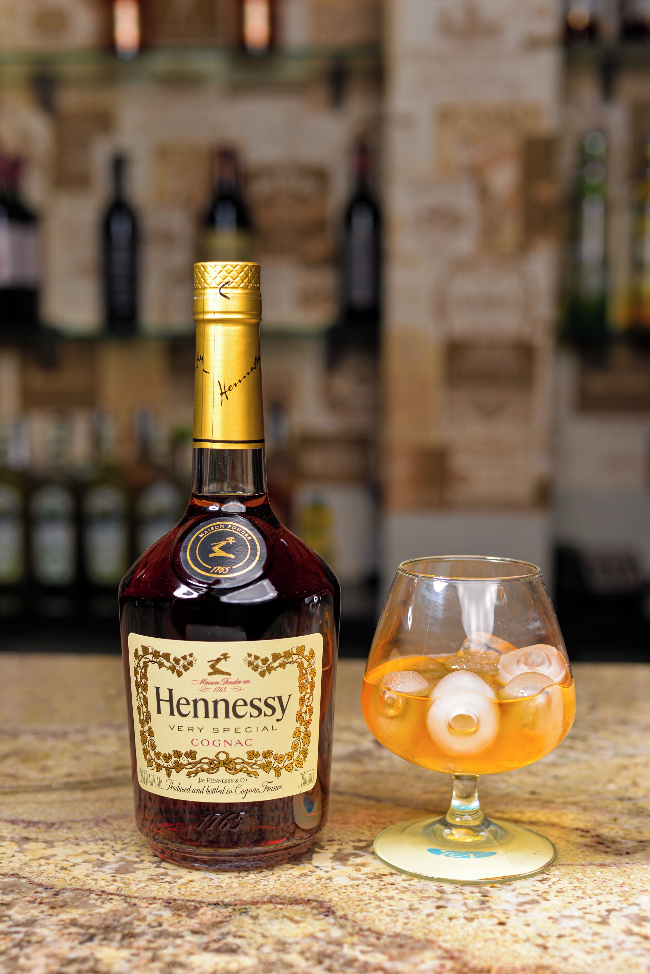 Une bouteille de cognac Hennessy et un verre rempli de glaçons, posés sur un comptoir.