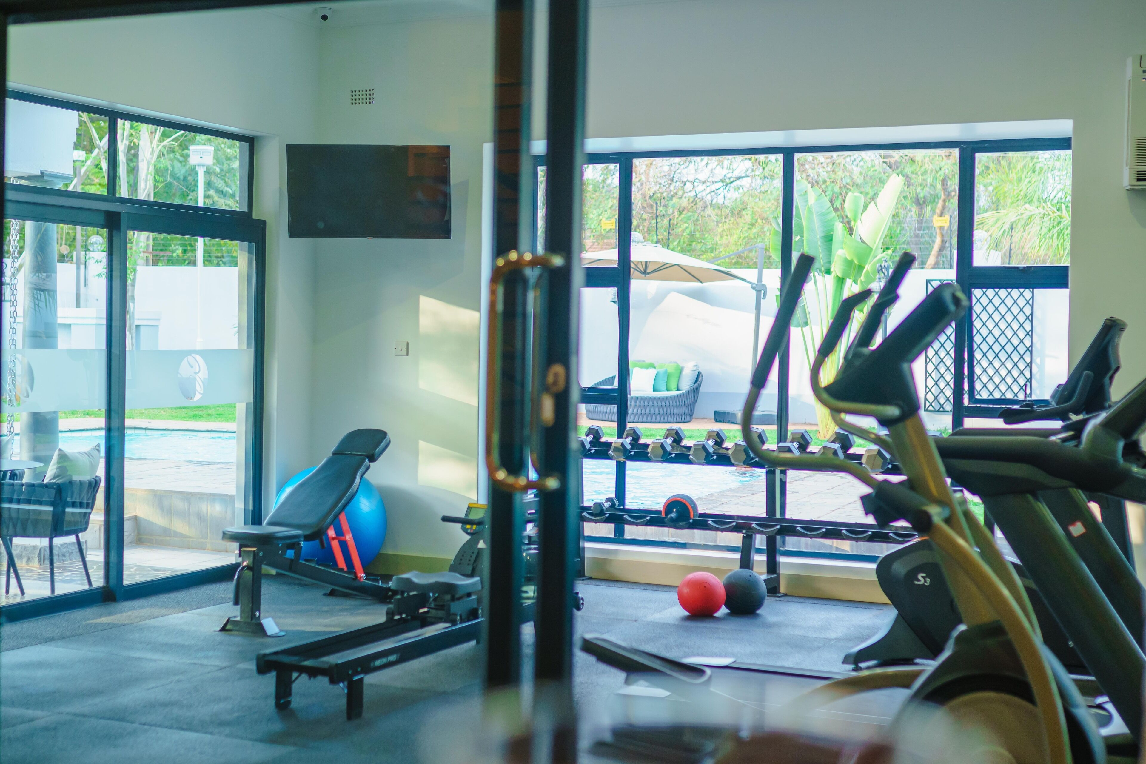 Un gimnasio con equipo de ejercicio, una banca y vistas al exterior a través de amplias ventanas.