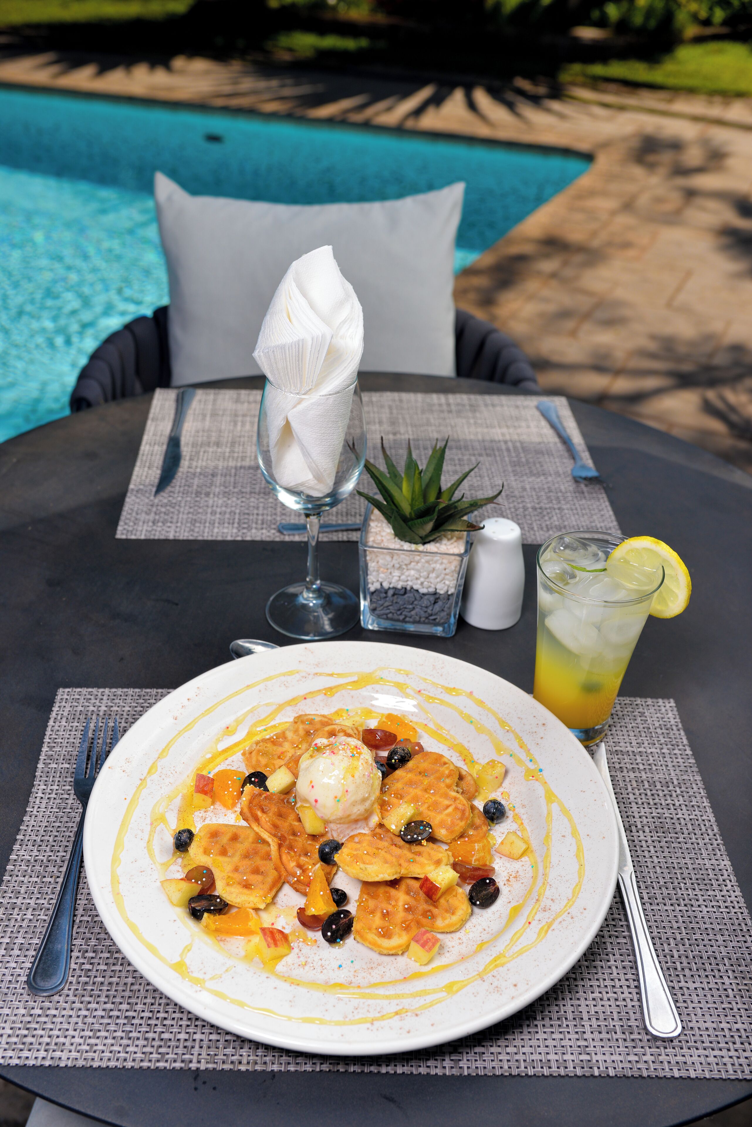 A dining table with a plate of food, a glass of drink, and a small plant.