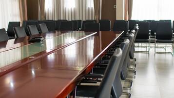Un salón de conferencias con una mesa larga y sillas, ventanas amplias con cortinas y suelo de baldosas.