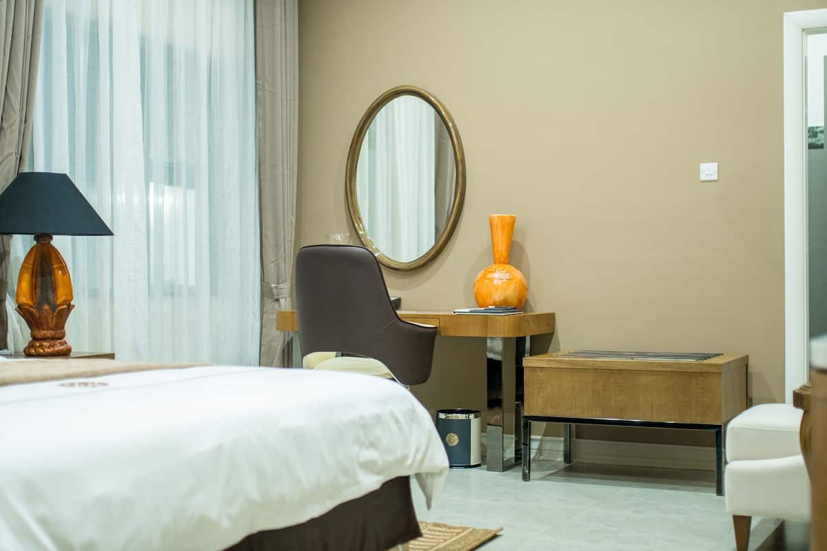 Een hotelkamer met een bed, bureau, stoel, spiegel en vaas.