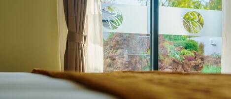 Een hotelkamer met een bed, gordijnen en een raam met uitzicht op groen en bomen.