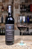 Una botella de vino Meerlust Rubicon y una copa de vino tinto sobre una encimera de mármol.