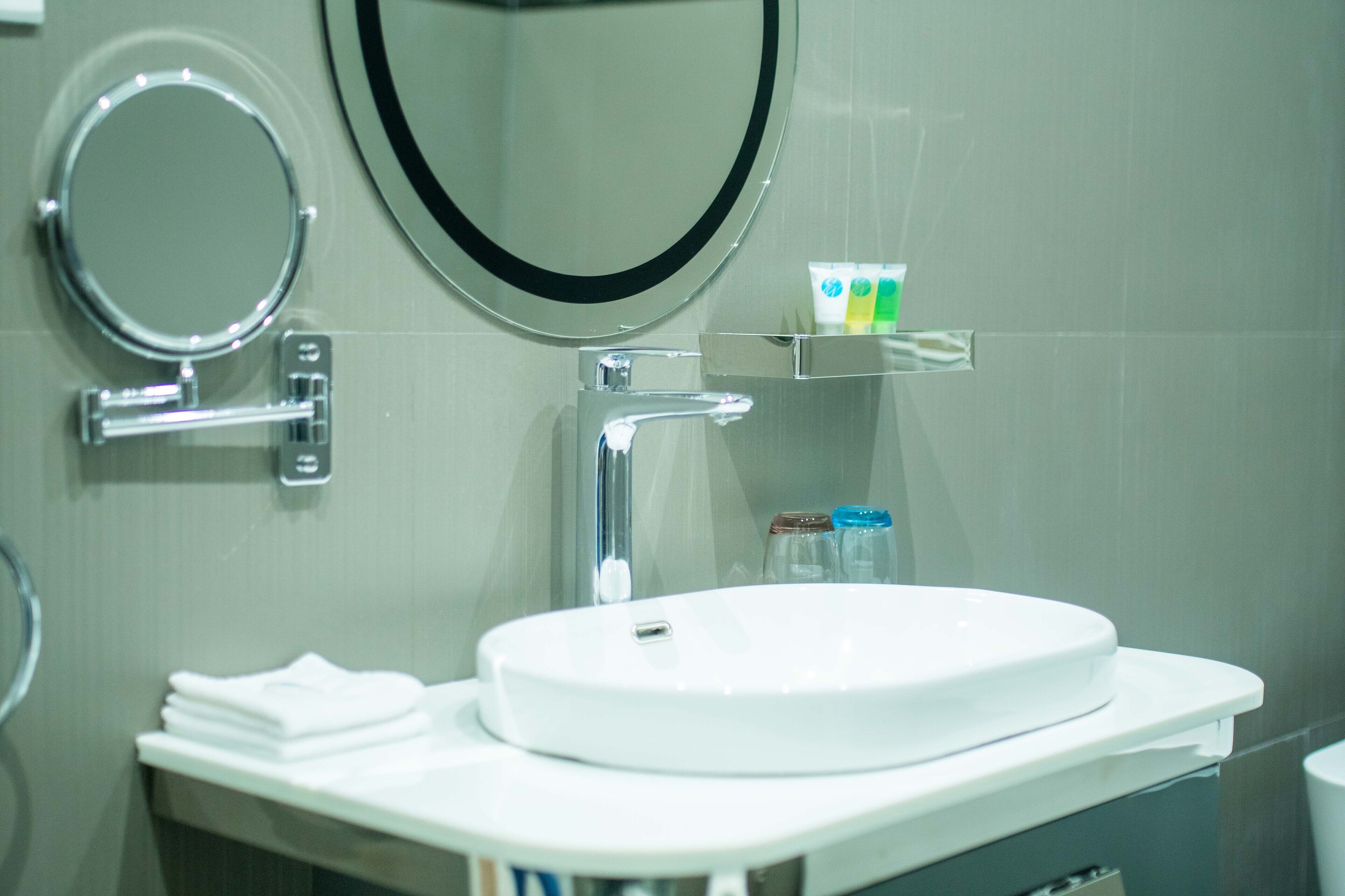 A bathroom with a white sink, a round mirror, and a soap dispenser on a shelf.