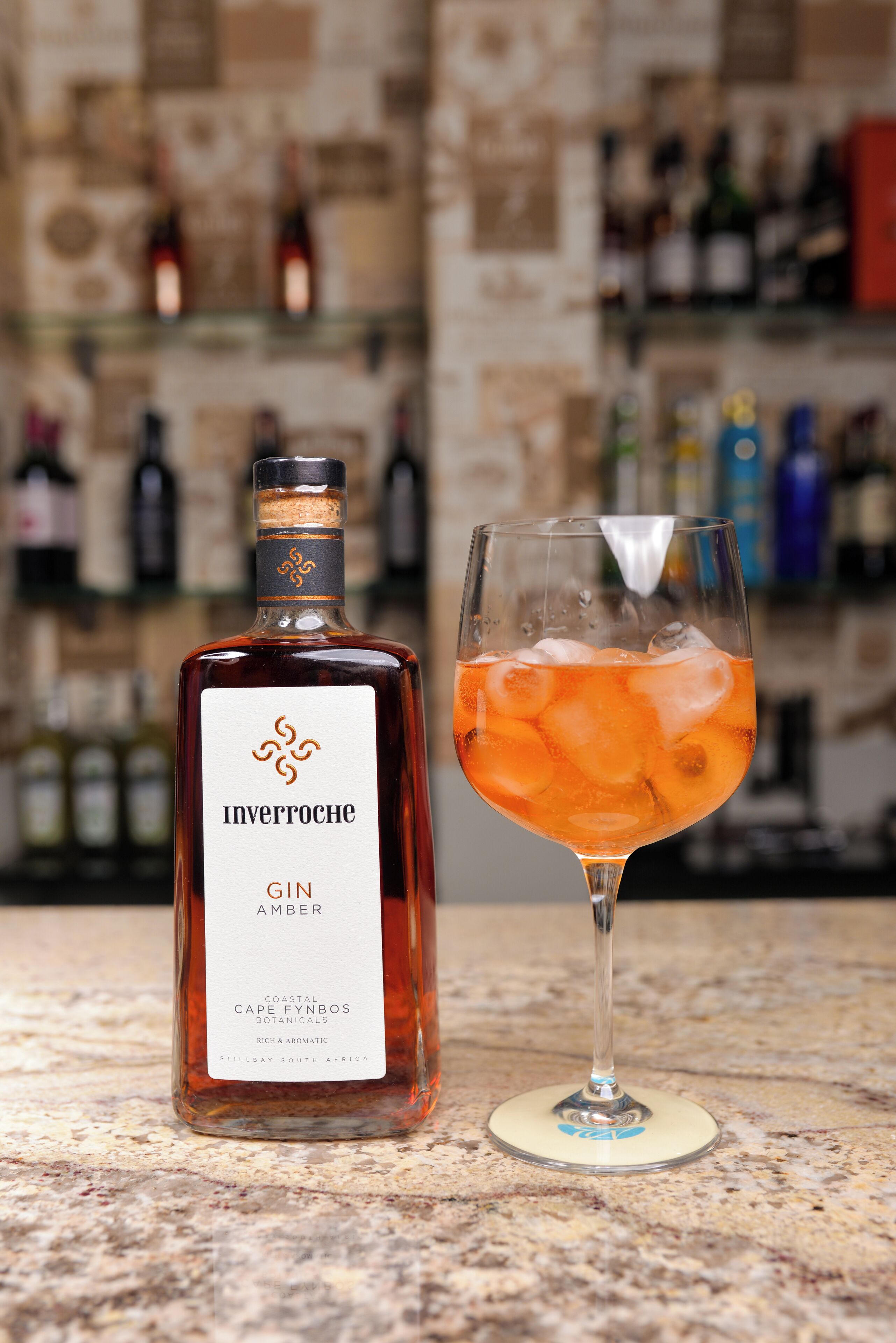 Une bouteille de gin Invergowne et un verre contenant une boisson à l’orange, posés sur le comptoir d’un bar.
