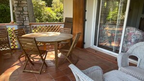 A patio with a round wooden table and chairs, a wicker chair, and a view through a sliding glass door.