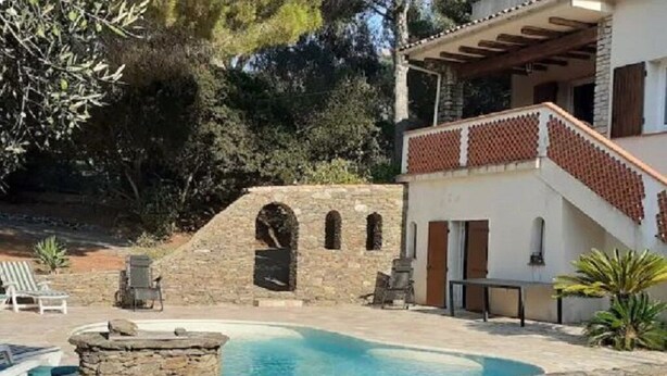 A pool area with stone walls, a stone archway, and a building with a red-tiled roof.