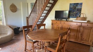 A dining area with a wooden table and chairs, a television on a cabinet, and a staircase.