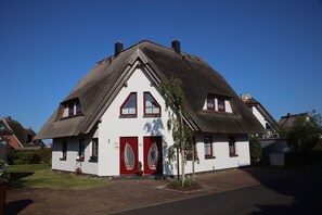 Et traditionelt hus med et stejlt stråt ækt tag, hvide vægge og røde døre.
