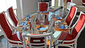 Un coin repas avec une table en verre entourée de chaises rouges et blanches, agrémenté d’assiettes, de tasses et d’un verre, le tout dans des tons de bleu et de blanc.