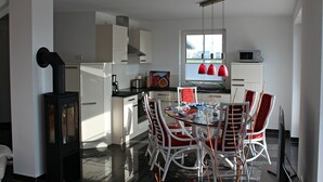 Une cuisine moderne avec des meubles blancs, une cuisinière et un coin repas comprenant des chaises blanches et une table en verre.