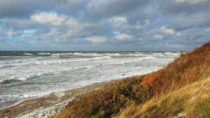 Un paysage côtier où les vagues s’écrasent sur une plage rocheuse, sous un ciel nuageux.